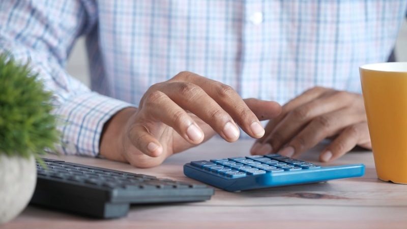 Manos usando una calculadora junto a un portátil